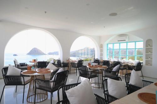 a dining room with tables and chairs and windows at Loccal Collection Hotel Komodo in Labuan Bajo