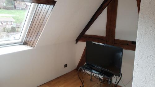 a flat screen tv sitting in a room with a window at GITE AU PETIT RUISSEAU-Etage et combles-maison alsacienne 4 personnes 4 nuitées minimum in Langensoultzbach