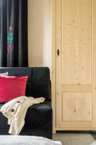 a black couch next to a wooden door with a red pillow at Highlander Heart Residence in Zakopane