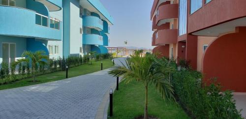 a walkway between two apartment buildings with palm trees at Golden Lake Apart Hotel Arraial do Cabo in Arraial do Cabo