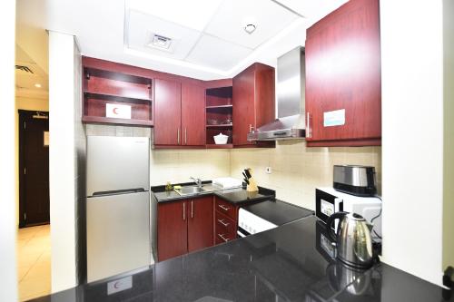 a kitchen with wooden cabinets and a stainless steel refrigerator at Luxury Escapes - Budget Studio with Garden Views near Metro - MED64 DG in Dubai