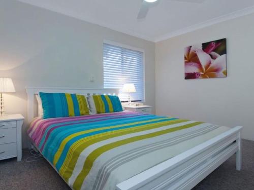 una camera bianca con un letto con una coperta a righe colorate di Bay Parklands 69 large unit with views pool tennis court and spa a Nelson Bay