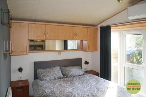 a bedroom with a bed and wooden cabinets and a window at Chalet/Caravan Camping Resort Heische Tip Zeeland in Zeeland