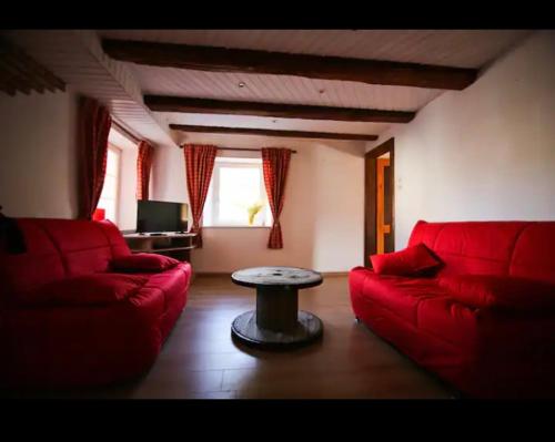 gite du heidenberg في Osenbach: غرفة معيشة بها كنبتين حمراء وطاولة