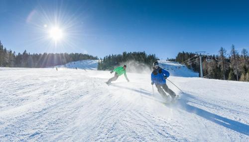 two people are skiing down a snow covered slope at Feriendorf Berghof in Villach