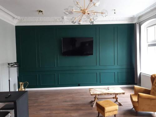 a living room with a green wall with a tv at Kamienica Bydgoska in Bydgoszcz