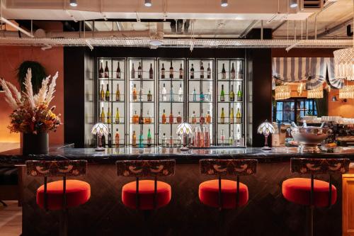 a bar with red chairs in front of a wall of alcohol bottles at room2 Chiswick Hometel in London