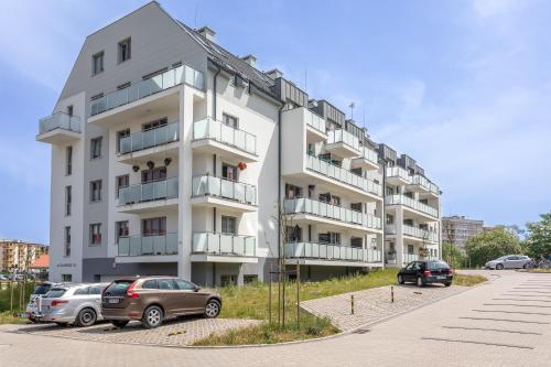 een wit appartementencomplex met auto's geparkeerd op een parkeerplaats bij Ambria Apartments Ułańska in Świnoujście