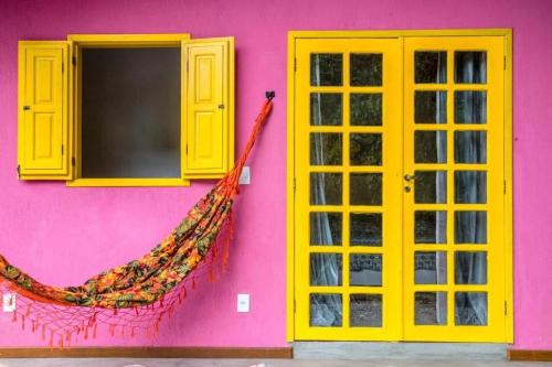 a pink building with yellow windows and a hammock on it at Bangalô Boa Ventura in Lumiar