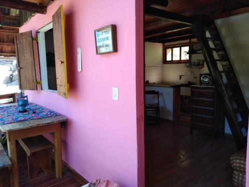 a pink wall in a room with a table and a kitchen at Bangalô Boa Ventura in Lumiar