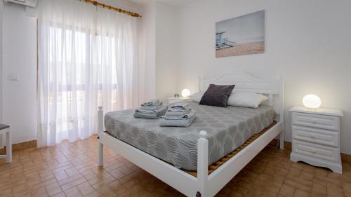 a white bedroom with a bed and a window at Apartamento T2 na Praia da Alagoa in Altura