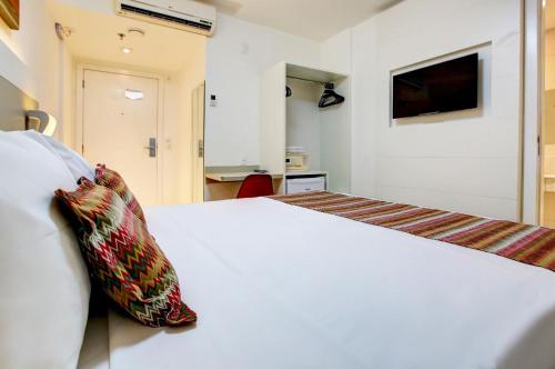 a bedroom with a white bed and a tv on the wall at Transamerica Fit Vitória Reta da Penha in Vitória