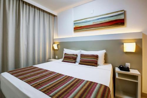 a hotel room with a white bed with two pillows at Transamerica Fit Vitória Reta da Penha in Vitória