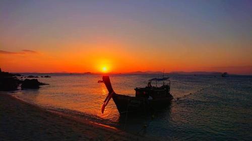 Ein Boot liegt bei Sonnenuntergang am Strand. in der Unterkunft Activities Resort in Ko Yao Yai