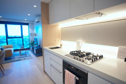 a kitchen with a stove top oven next to a living room at Box Hill Central Sky One Apartment in Box Hill