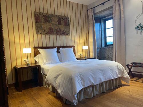 a bedroom with a bed with white sheets and two lamps at Rectoral de Cines in Oza dos Ríos