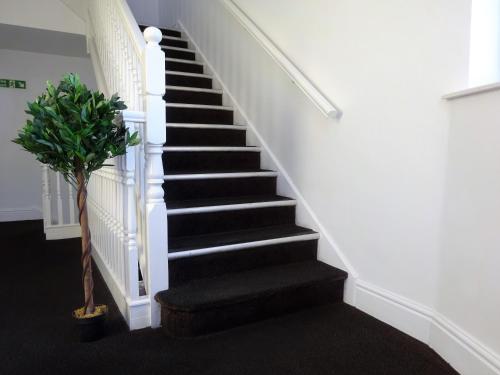 a staircase with black carpeting and white stairs with a plant at Wigan Central I 1 & 2 Bed Executive Apartments I Family Rooms I Private Balcony I Free Parking in Wigan