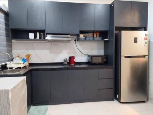 eine Küche mit schwarzen Schränken und einem Kühlschrank aus Edelstahl in der Unterkunft Yong Guesthouse in Kuala Kangsar
