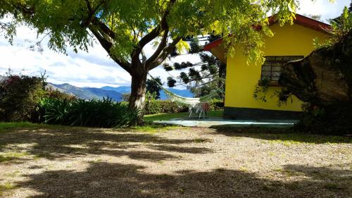 a yellow house with a hammock next to a tree at chales azaleia todos in São Bento do Sapucaí