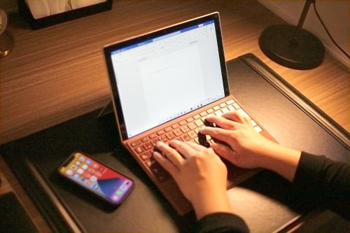 a person typing on a laptop computer with a cell phone at goom Hotel Fukuoka-Kokusai-Center in Fukuoka