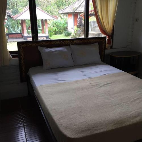 a bed with white sheets and pillows in front of a window at Villa Sinta in Baturiti