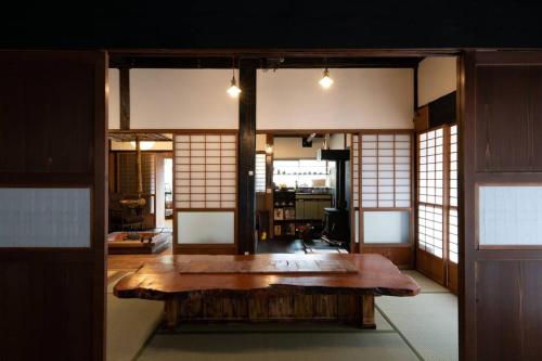a room with a wooden table in a room with windows at 囲炉裏つき古民家を丸ごと貸し切り「月夜見山荘」（庭にBBQグリル完成！） in Hayakawa