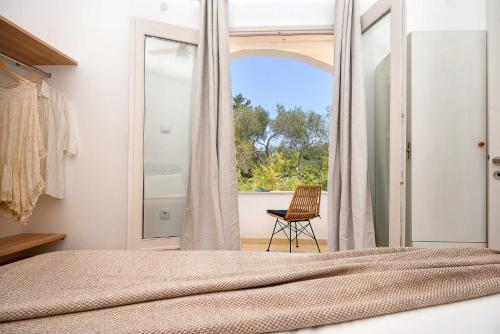 a bedroom with a bed and a window with a chair at PaxosBlue Suites & Villas in Gaios