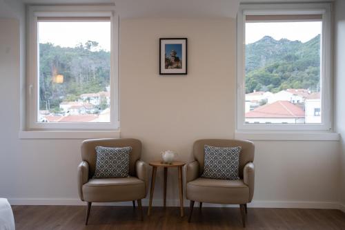 two chairs and a table in a room with two windows at Beecaramulo-Apiturismo in Caramulo