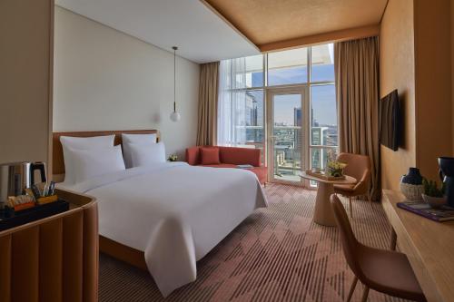 Cette chambre comprend un grand lit blanc et une grande fenêtre. dans l'établissement Novotel Jumeirah Village Triangle, à Dubaï