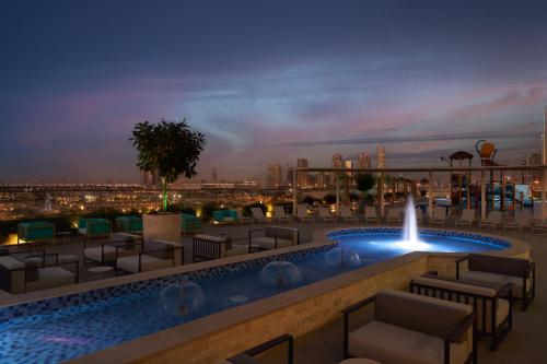 Novotel Jumeirah Village Triangle في دبي: مسبح على السطح مع كراسي ونافورة في الليل