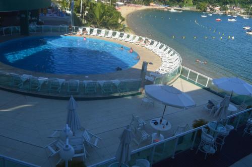 uma grande piscina ao lado de uma praia com guarda-sóis em Angra Praia Grande Flat Studio Angra Inn - O Mar de Angra te espera ! em Angra dos Reis