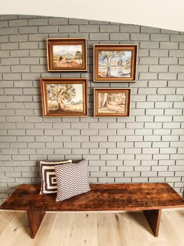 a brick wall with a wooden bench and framed pictures at RIVERLEA RETREAT MUDGEE - Private, Outdoor Bath, Pool, Tranquility in Apple Tree Flat