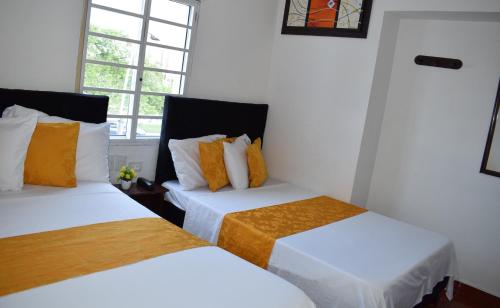 two beds in a room with white and orange pillows at Hotel Avenida 3 Real en el norte de Cali in Cali