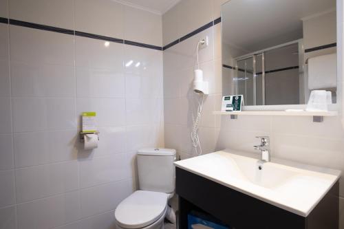 a white bathroom with a toilet and a sink at Hotel Le Beffroi in Dreux