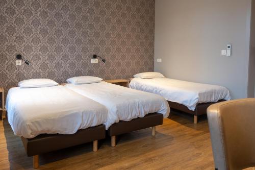 a room with two beds with white sheets at Oud Gemeentehuis in Poelkapelle