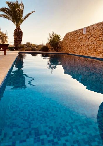 a swimming pool with blue water and a palm tree at Sunset Farmhouse in Għarb