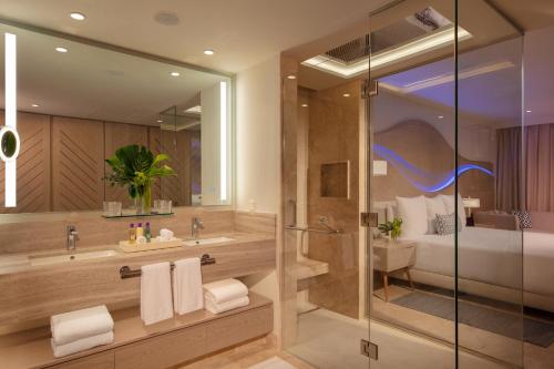 a bathroom with a shower and a sink and a bed at Breathless Cancun Soul Resort & Spa - Adults Only - All Inclusive in Cancún