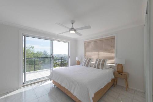 a white bedroom with a bed and a large window at Dreamtime Beach Retreat in Forster