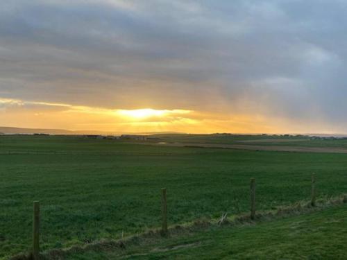 a fence in a field with the sunset in the background at Loanside Lodge, Self-Catering, Holm, Orkney. in Saint Marys