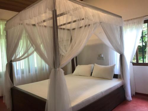 a bedroom with a canopy bed with white curtains at Eco Willow - Kathaluwa in Atadahewatugoda