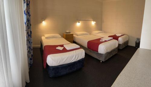a room with three beds with red and white sheets at Lake Munmorah Motel in Lake Munmorah