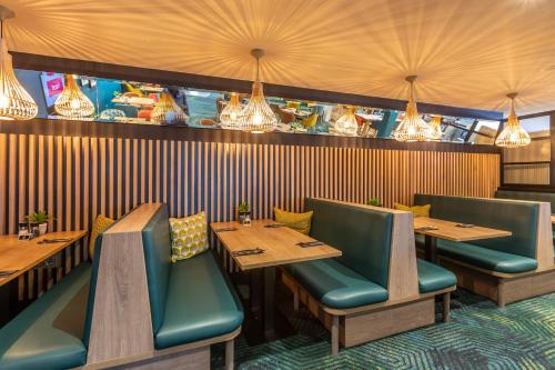 a restaurant with wooden tables and green chairs at Holiday Inn Oxford by IHG in Oxford
