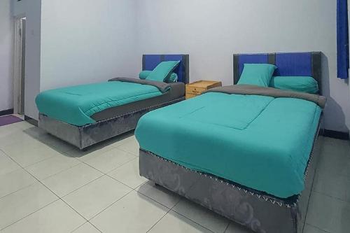 two twin beds in a room with blue sheets at Angrumba Family Homestay near RSUD Caruban Mitra RedDoorz in Mejayan