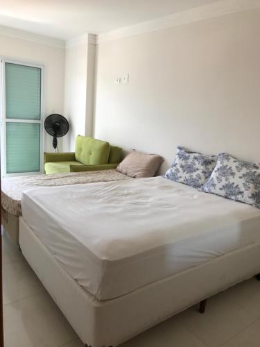uma grande cama branca num quarto com uma cadeira verde em Apto super confortável 1 quadra da praia Wi-Fi 02 banheiros Churrasqueira na sacada na Praia Grande