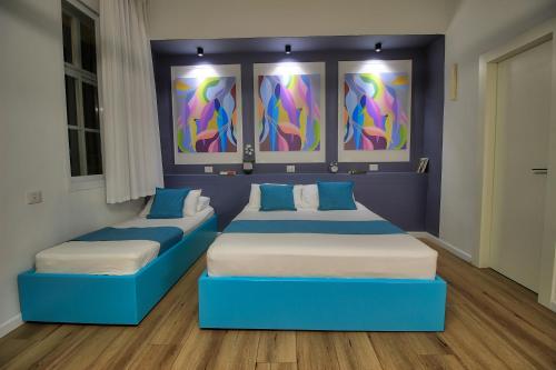two blue beds in a room with paintings on the wall at 1926 Designed ApartHotel in Haifa