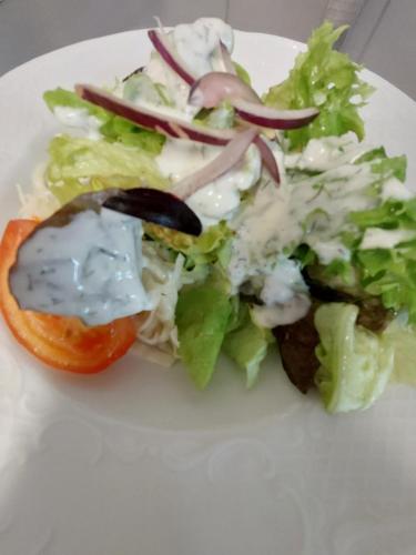 a salad with a tomato and dressing on a white plate at Cross-Country-Hotel Hirsch in Sinsheim