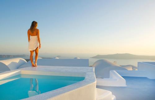 a woman in a white dress standing on a ledge next to a pool at Avista Suites in Imerovigli