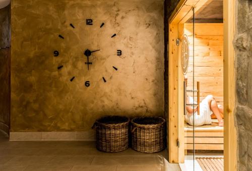 a person sitting on a bed in a room with a clock on the wall at Das Aunhamer Suite & Spa Hotel in Bad Griesbach