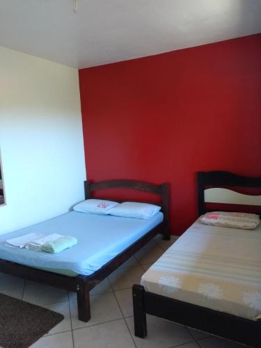 two beds in a room with a red wall at Wando Suítes in Búzios