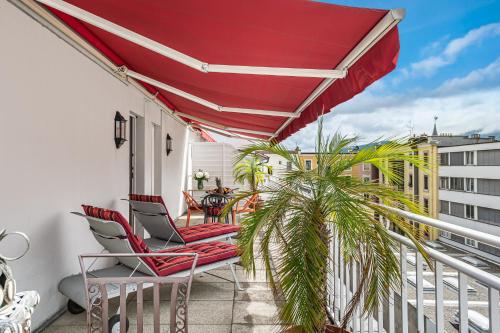 un balcón con 2 sillas y una sombrilla roja en Kipling Manotel en Ginebra